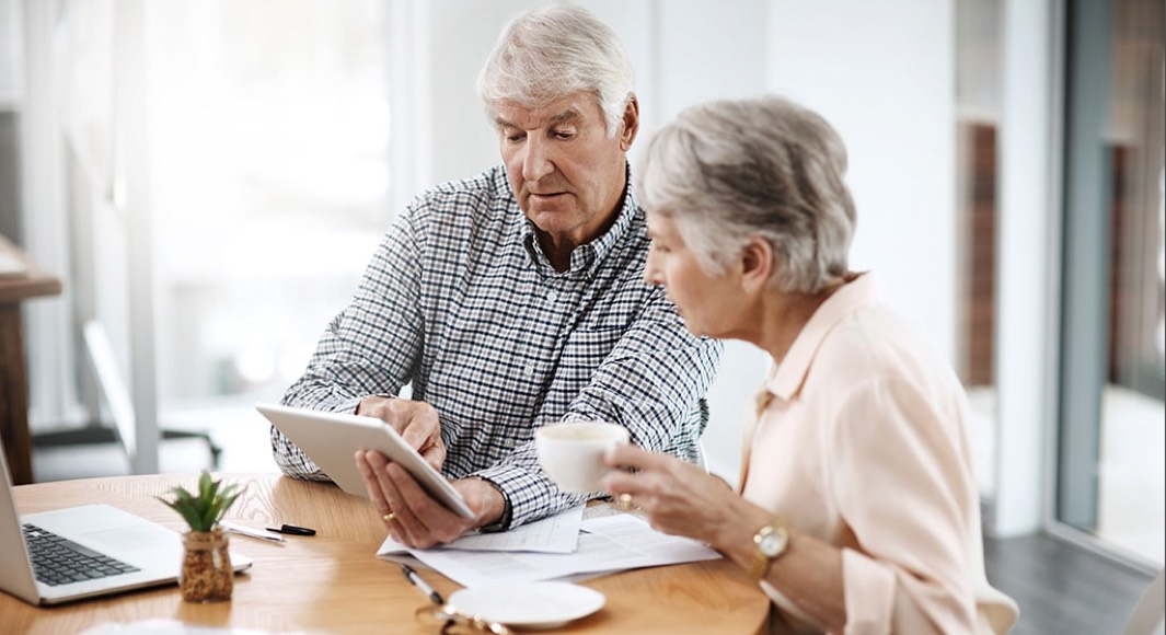 Older husband and wife looking at a tablet while drinking coffee